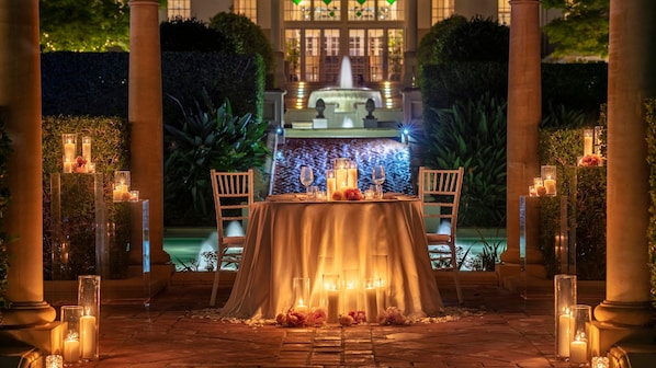 An outdoor dining area with a table set for two, surrounded by candlelit columns and a fountain in the background. - InterContinental Sanctuary Cove Resort by IHG (Hope Island)