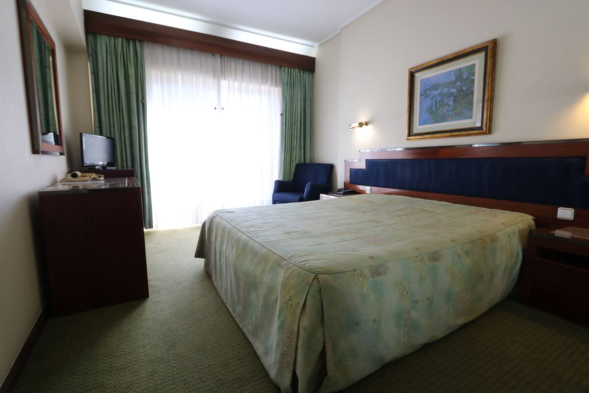 A hotel room with a large bed, a desk with a computer, a chair, a television, and a painting on the wall.