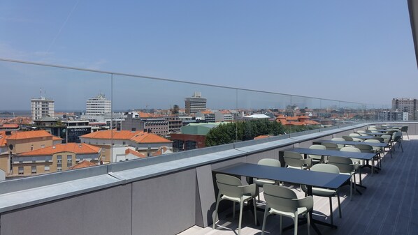 A rooftop terrace with tables and chairs, offering a view of a cityscape with various buildings. - Hotel Imperial (Aveiro)