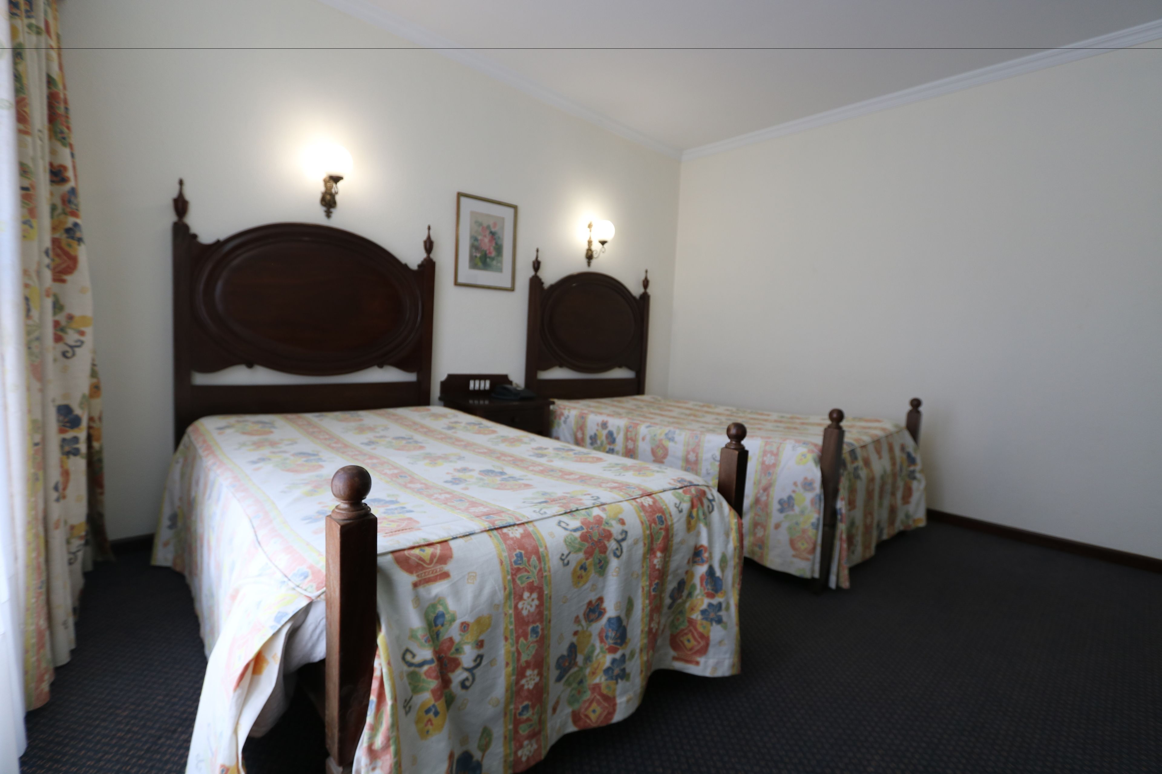 A hotel room with two wooden beds, each with a floral bedspread and headboard lamps.