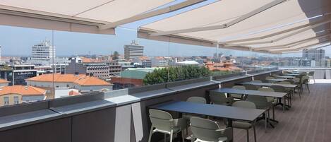 A rooftop terrace with tables and chairs, offering a view of the cityscape.