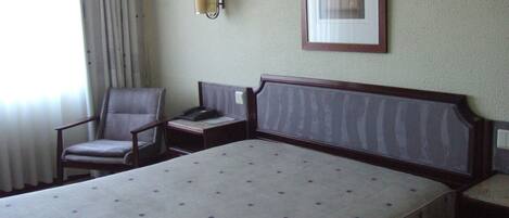 A hotel room with a large bed, a chair, a bedside table with a lamp, and a framed picture on the wall.