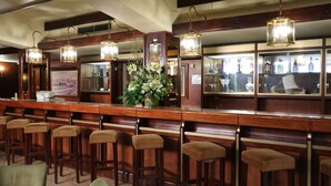 Zona de bar con taburetes de madera, lámparas colgantes y una exhibición de botellas de licor.