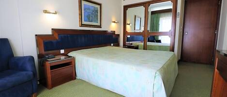 Una habitación de hotel con una cama, un escritorio, una silla, un espejo y una puerta.