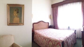 Habitación de hotel con una cama, una silla, un cuadro en la pared y una ventana con cortinas.