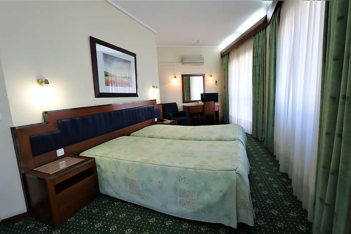 A hotel room with two beds, a desk, a chair, a mirror, and a picture on the wall.