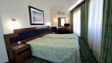 Quarto de hotel com duas camas, uma escrivaninha, uma cadeira, um espelho e um quadro na parede.