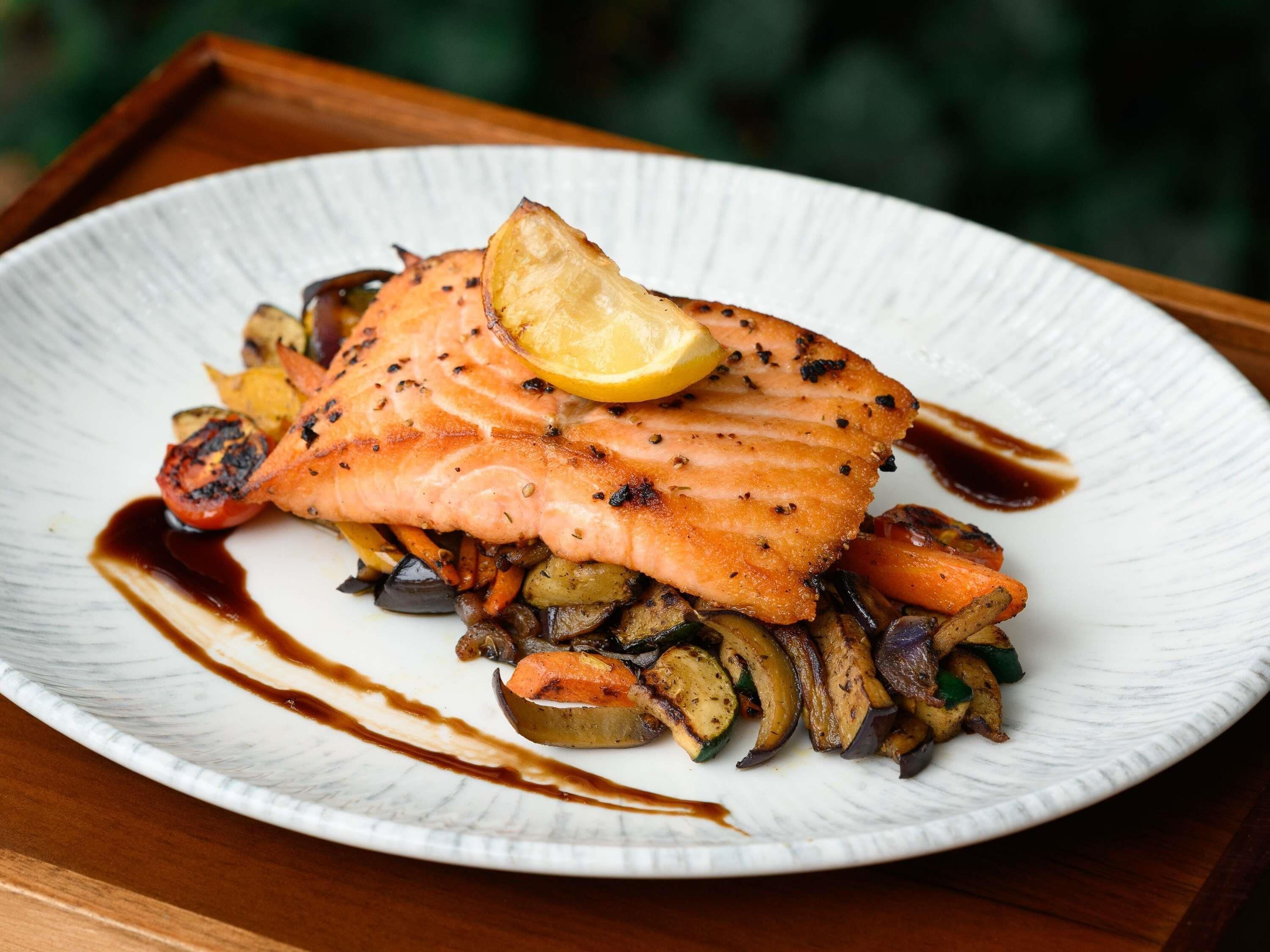 A plate of grilled salmon with vegetables and a lemon wedge.