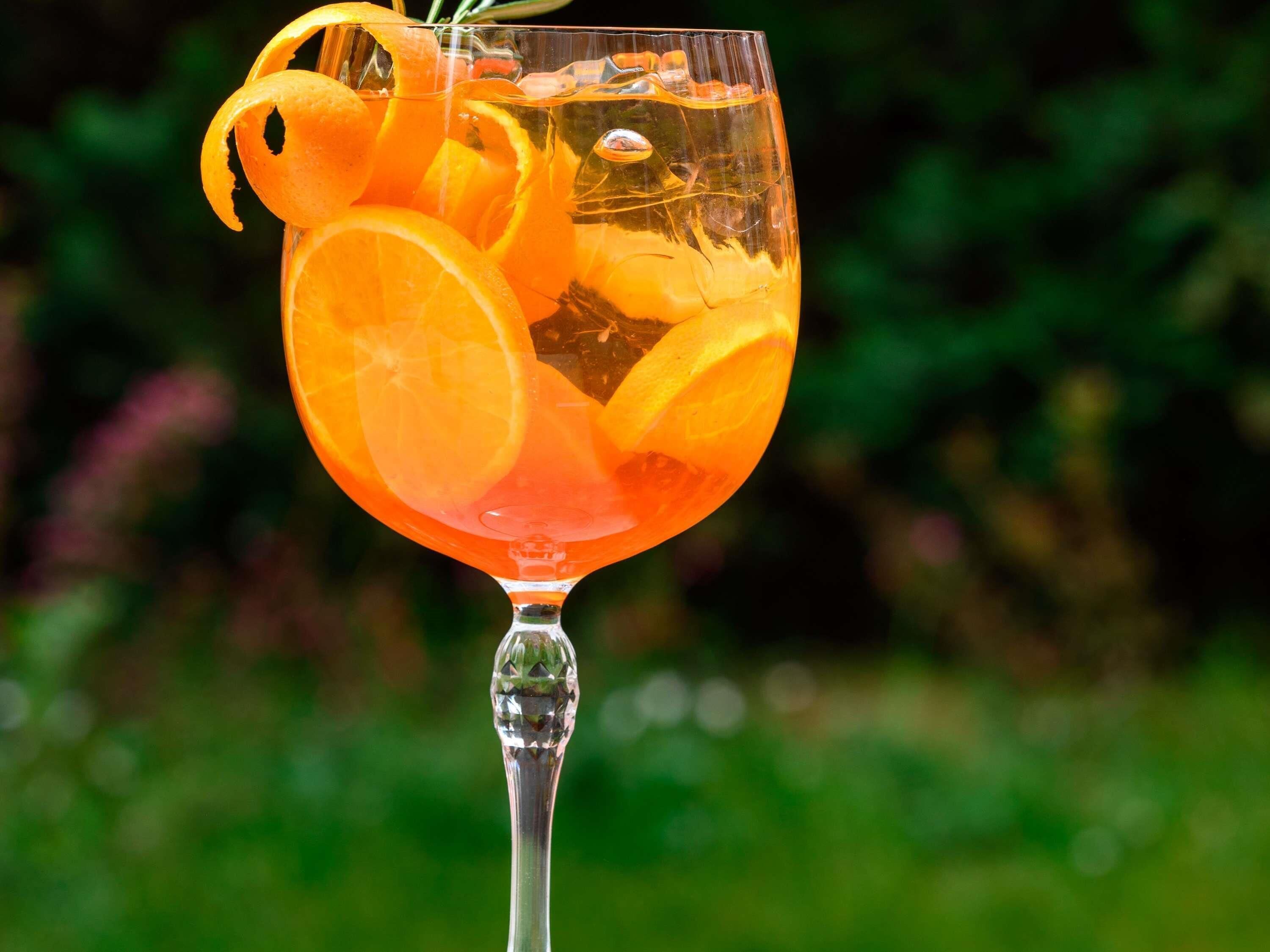 A cocktail glass with orange slices and a garnish, set against a blurred green background.