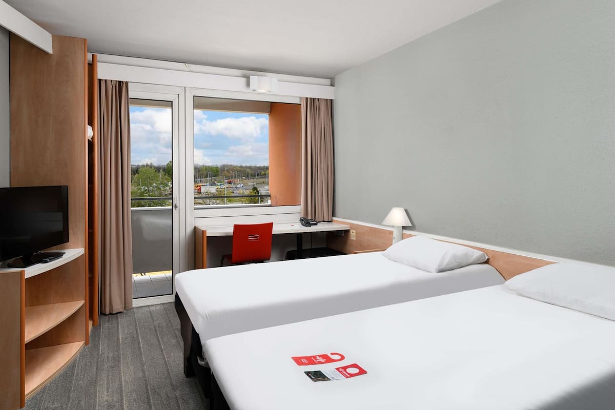 Habitación de hotel con cama, escritorio, televisor y vistas al exterior.
