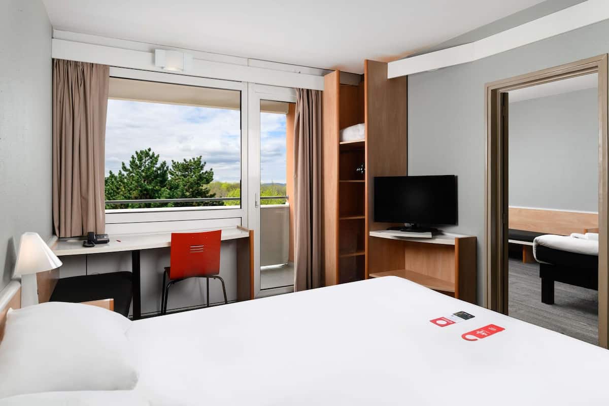 Una habitación de hotel con cama, escritorio, silla, televisión y armario.