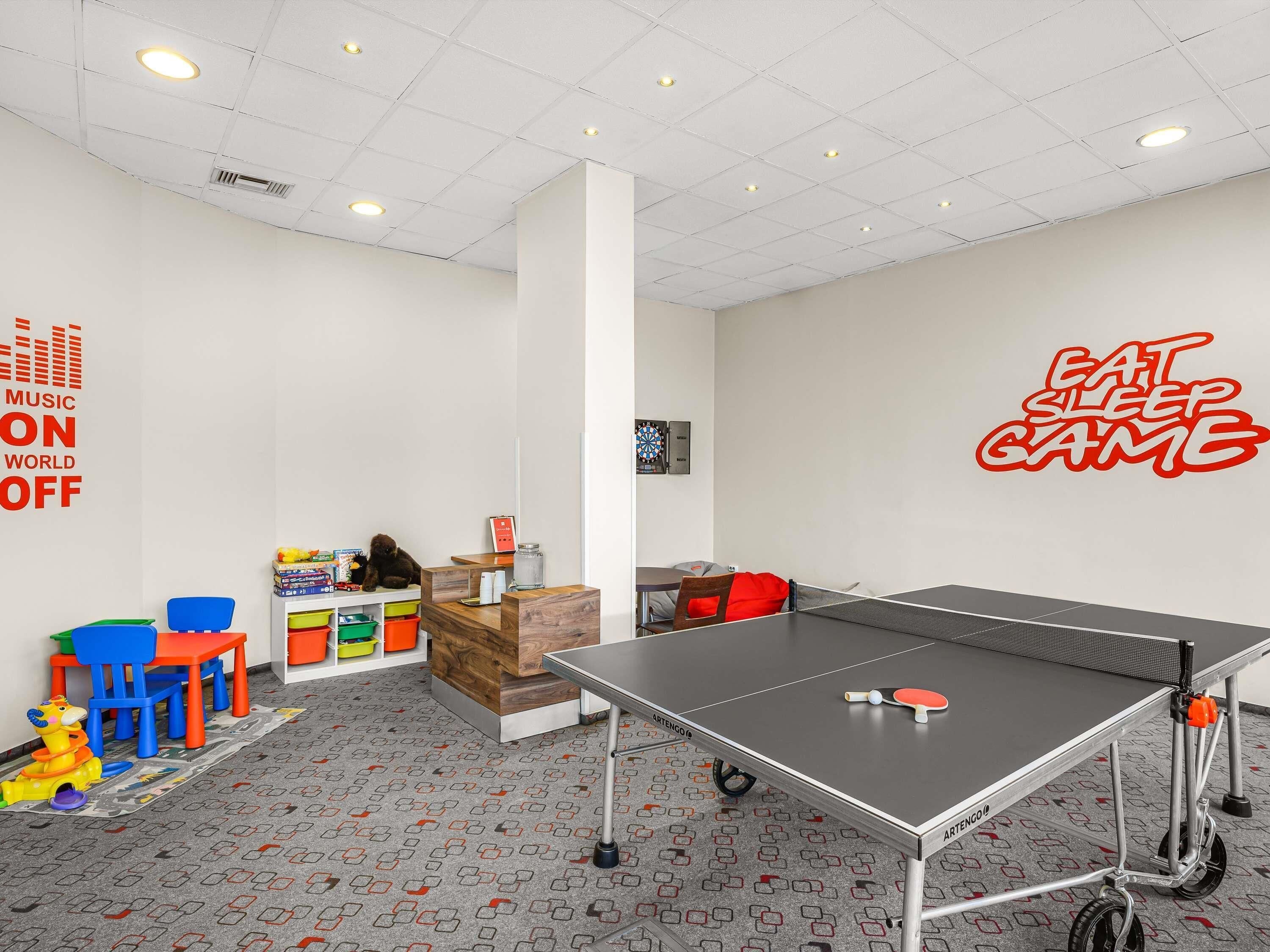 Una mesa de ping pong, sillas coloridas, un dardo y un tablero de dardos en la pared.