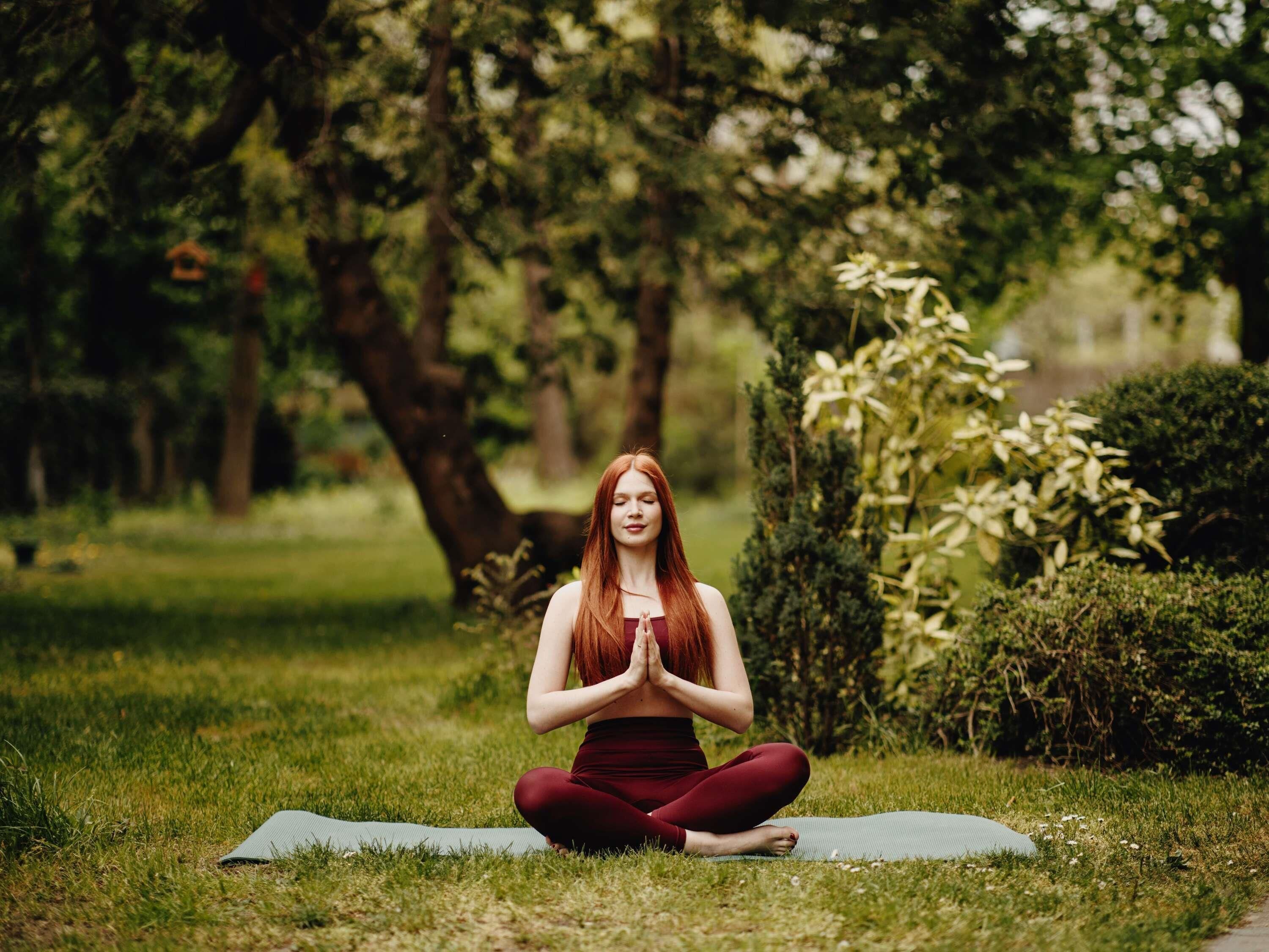 Iemand zit op een yogamat in een park.