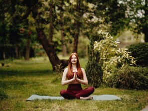 Una persona sentada sobre una colchoneta de yoga en un parque.