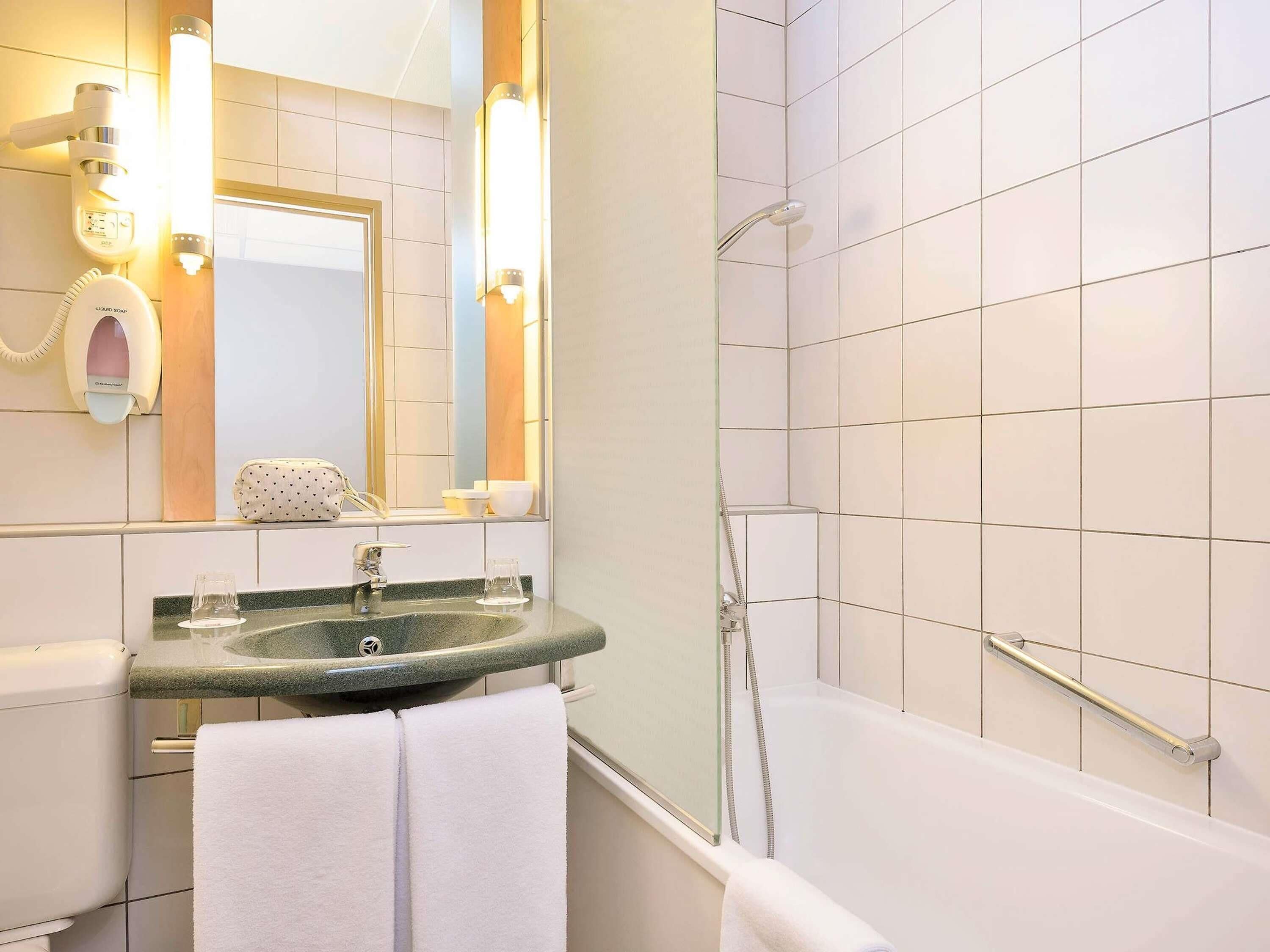 Un baño con lavamanos, espejo, toalla, ducha y barras de apoyo.
