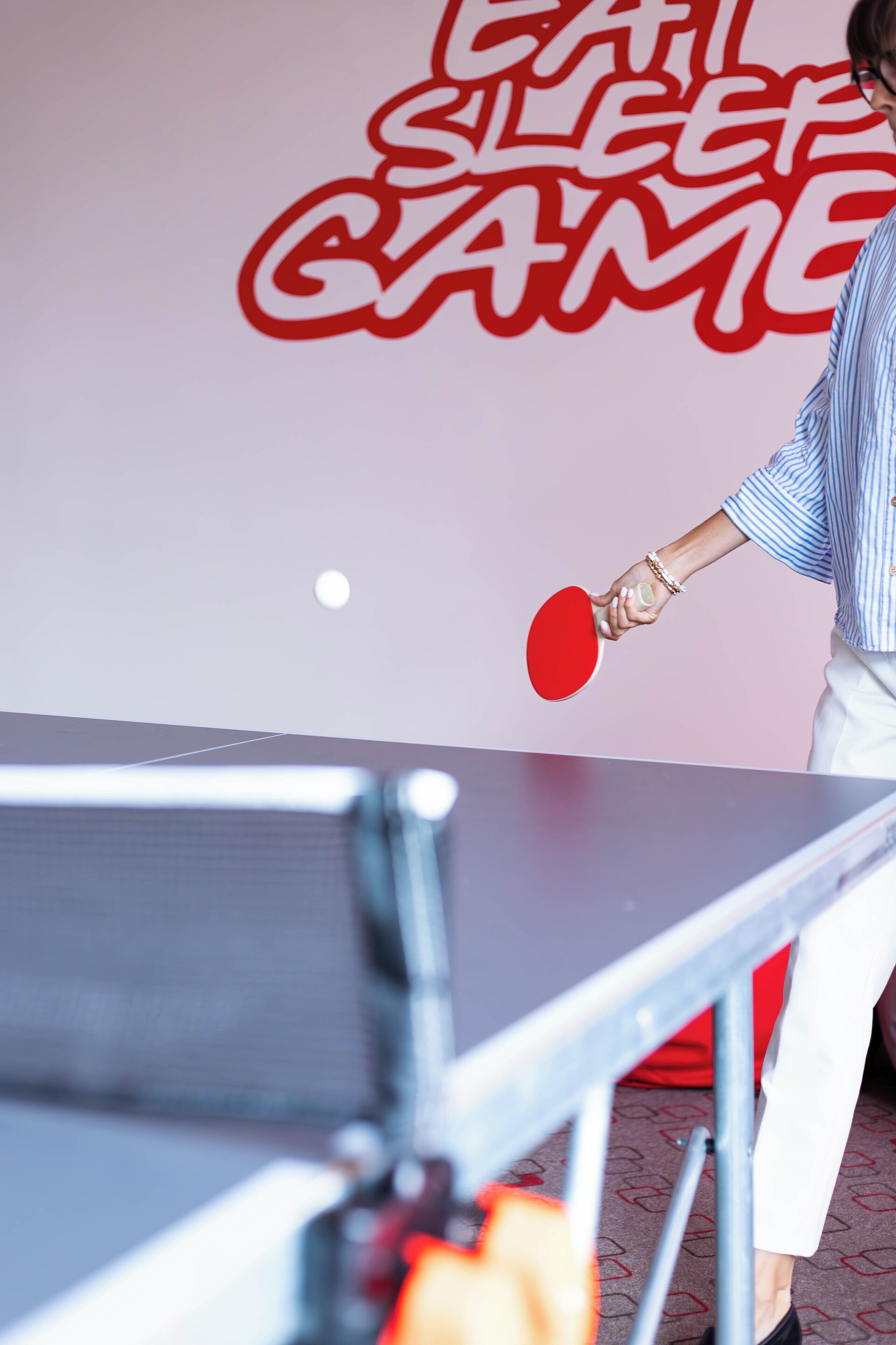 A table tennis table with a red paddle, a person playing, and a wall with red text.