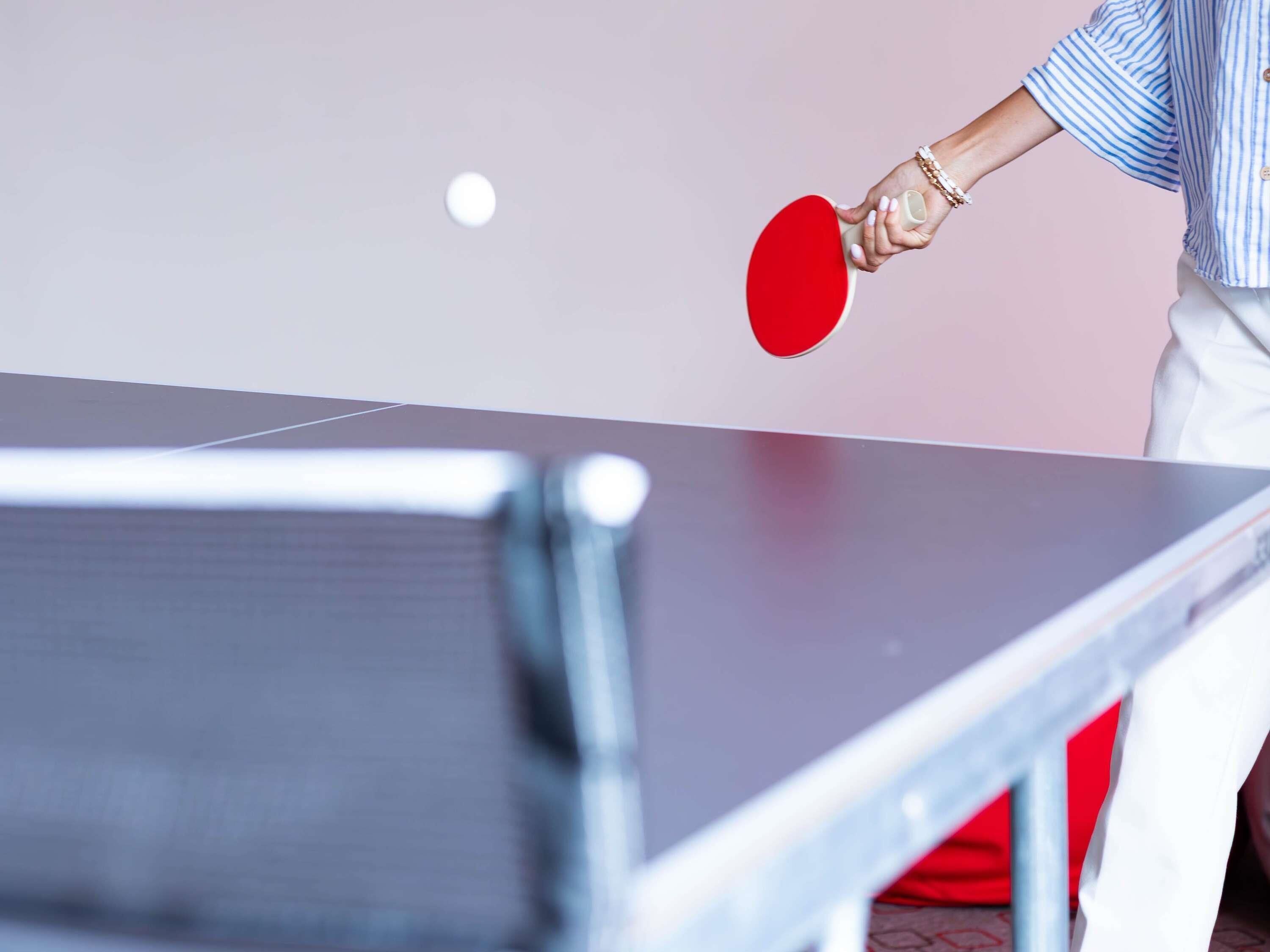 A table tennis table with a person holding a red paddle.