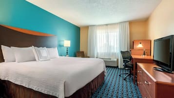Una habitación de hotel con una cama grande, un escritorio, una silla, un televisor y una ventana con cortinas.