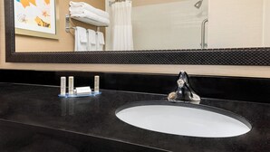 A bathroom with a black countertop, a white sink, and a large mirror. There are towels and toiletries on the counter.