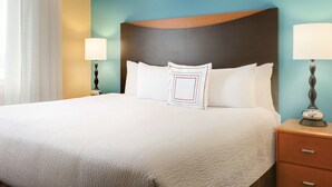 A neatly made bed with a textured white bedspread, a decorative pillow with a geometric pattern, and two bedside lamps on wooden nightstands.