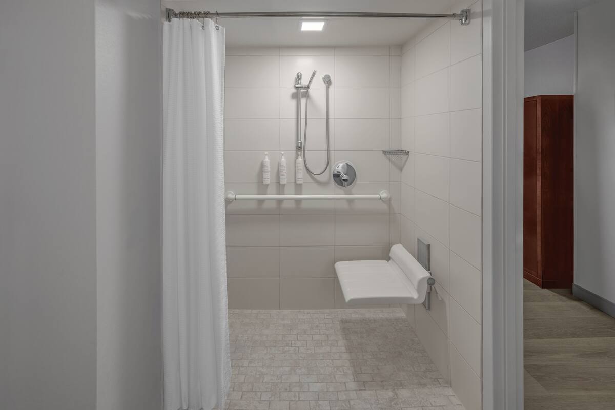 A modern bathroom with a shower, a towel rack, and a small shelf with toiletries.
