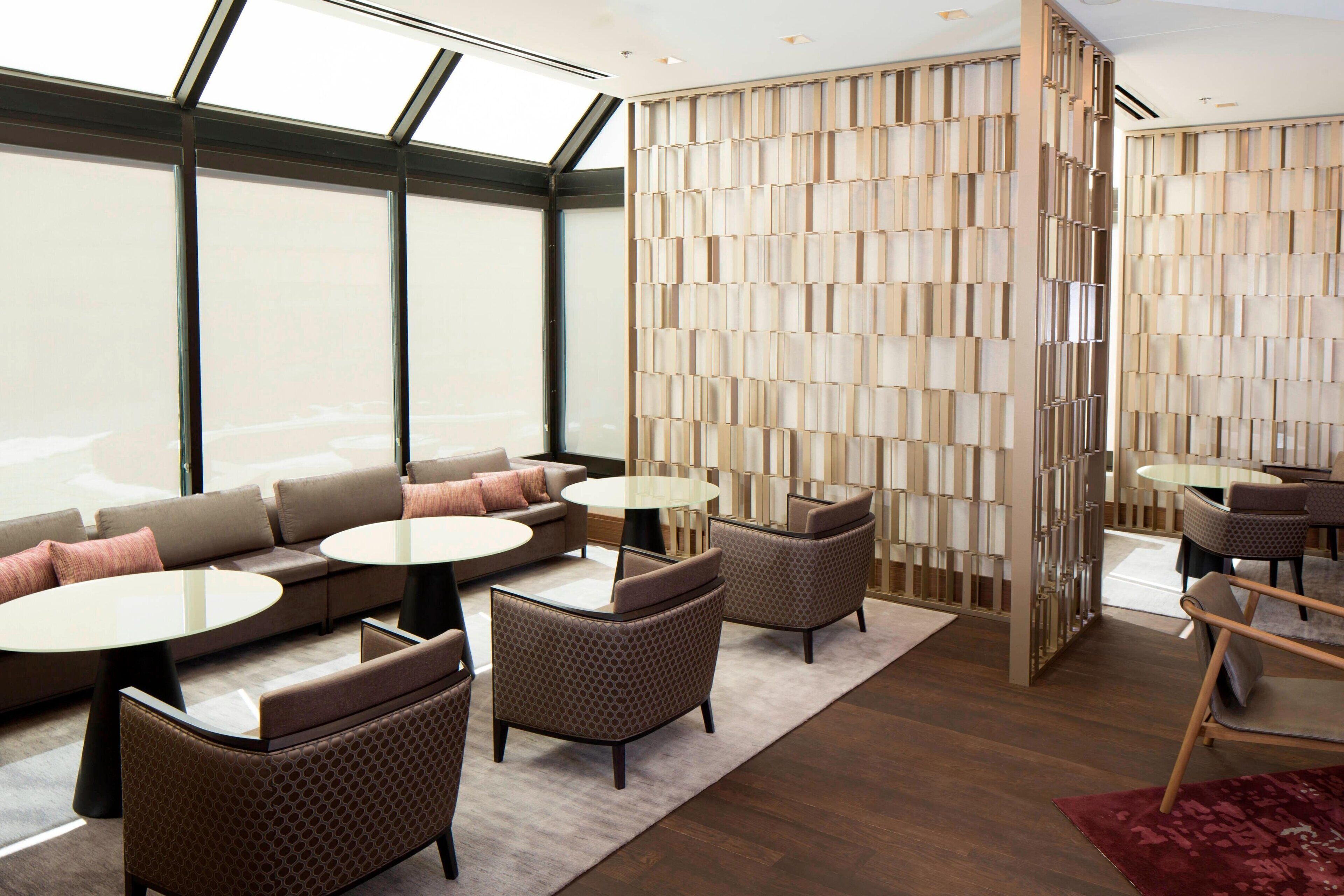 A modern hotel lobby with a large seating area, a decorative wall, and a view through large windows.