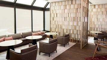A modern hotel lobby with a large seating area, a decorative wall, and a view through large windows.