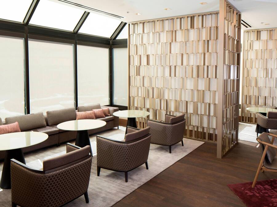 A modern hotel lobby with a large seating area, a decorative wall, and a view through large windows.