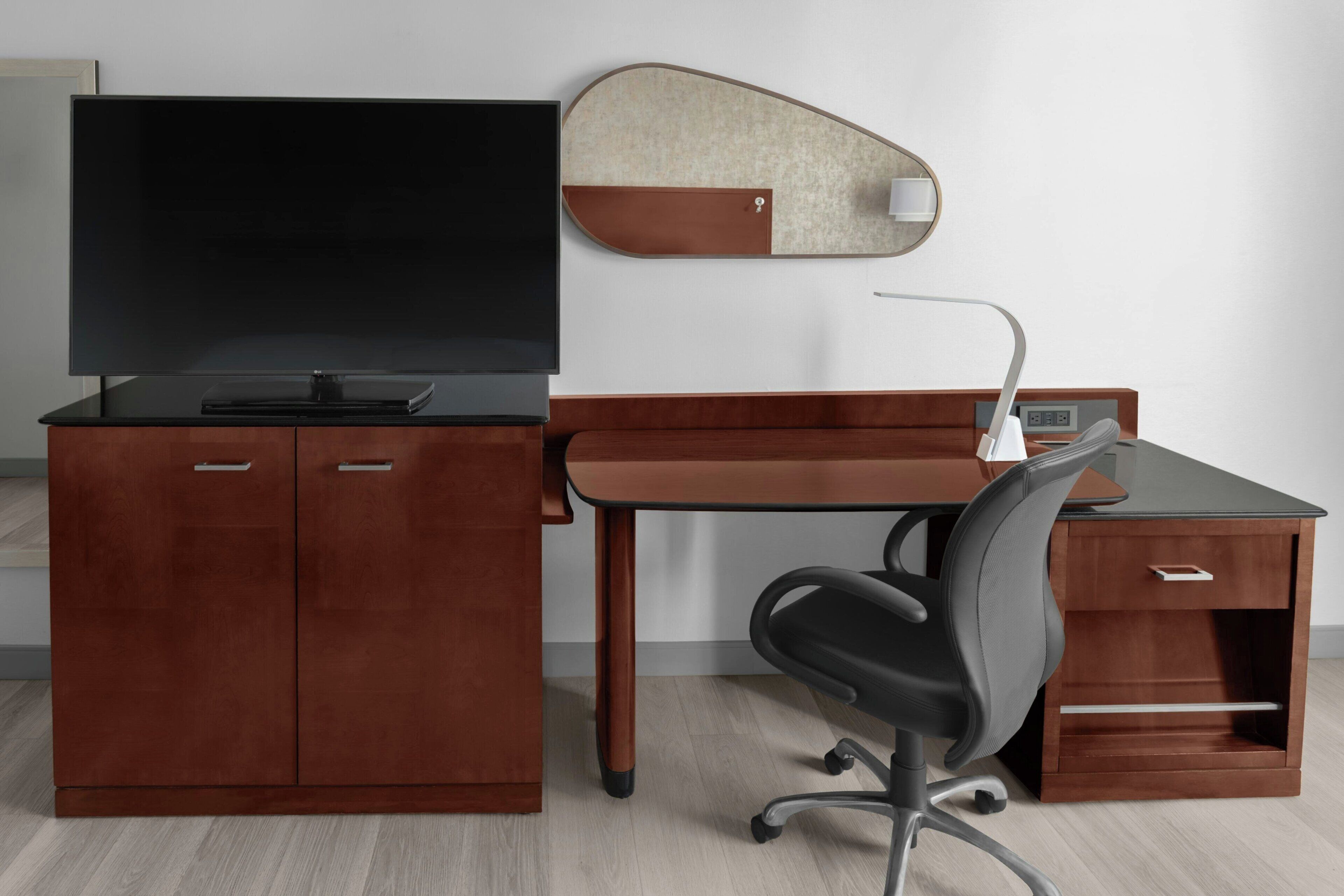 A modern office desk with a flat-screen TV, a desk lamp, and a chair.