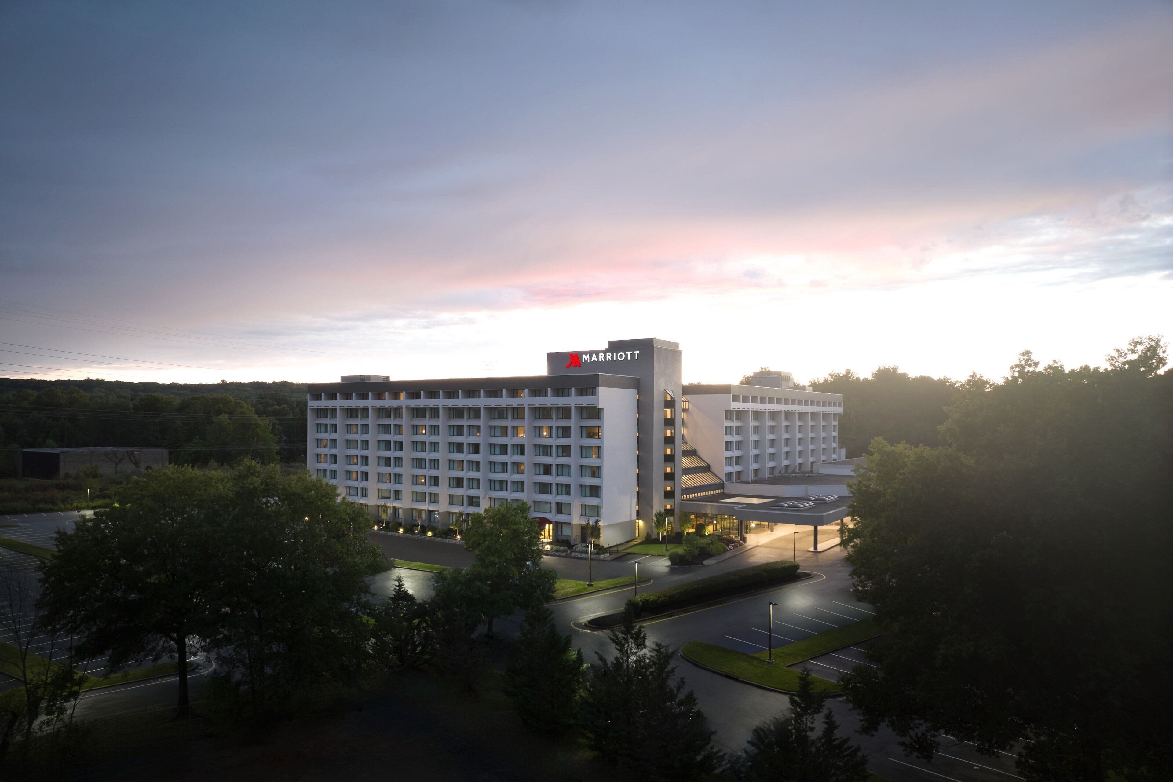 A Marriott hotel with a modern design, featuring a large building with multiple floors and a prominent sign. The hotel is surrounded by greenery and has a parking lot in front.