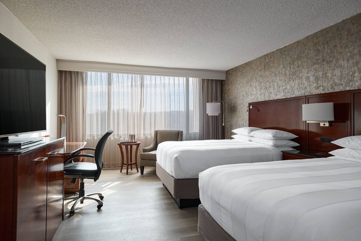A hotel room with two beds, a desk with a chair, a small table, and a television.