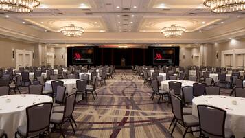 A large conference room with round tables and chairs, chandeliers, and a stage with a podium.