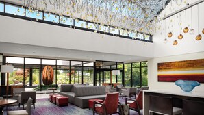 A spacious lobby with a large gray sofa, red chairs, a coffee table, and a modern art piece on the wall. - Hanover Marriott (Whippany)