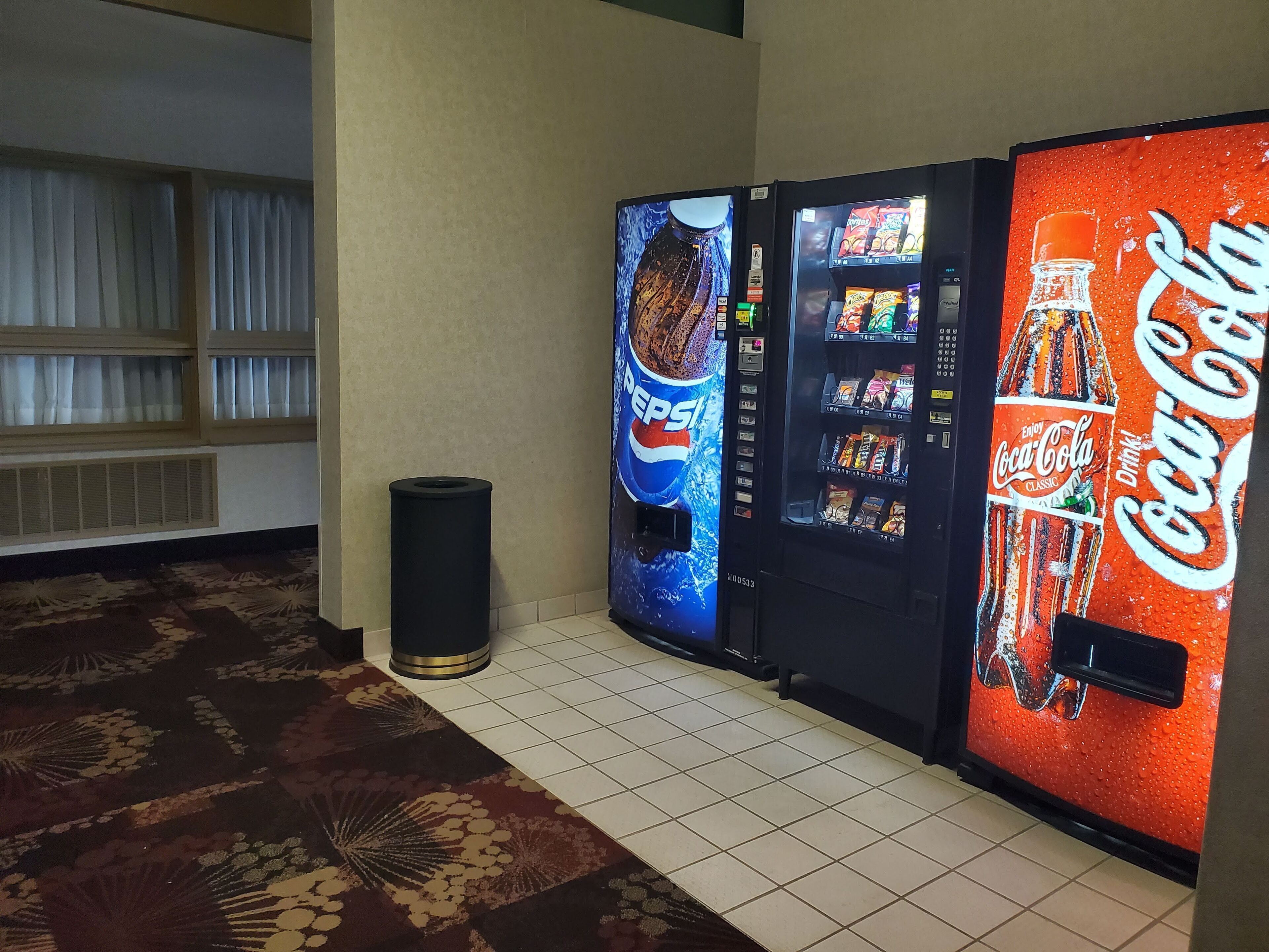 A hallway with vending machines, a trash can, and patterned carpet.