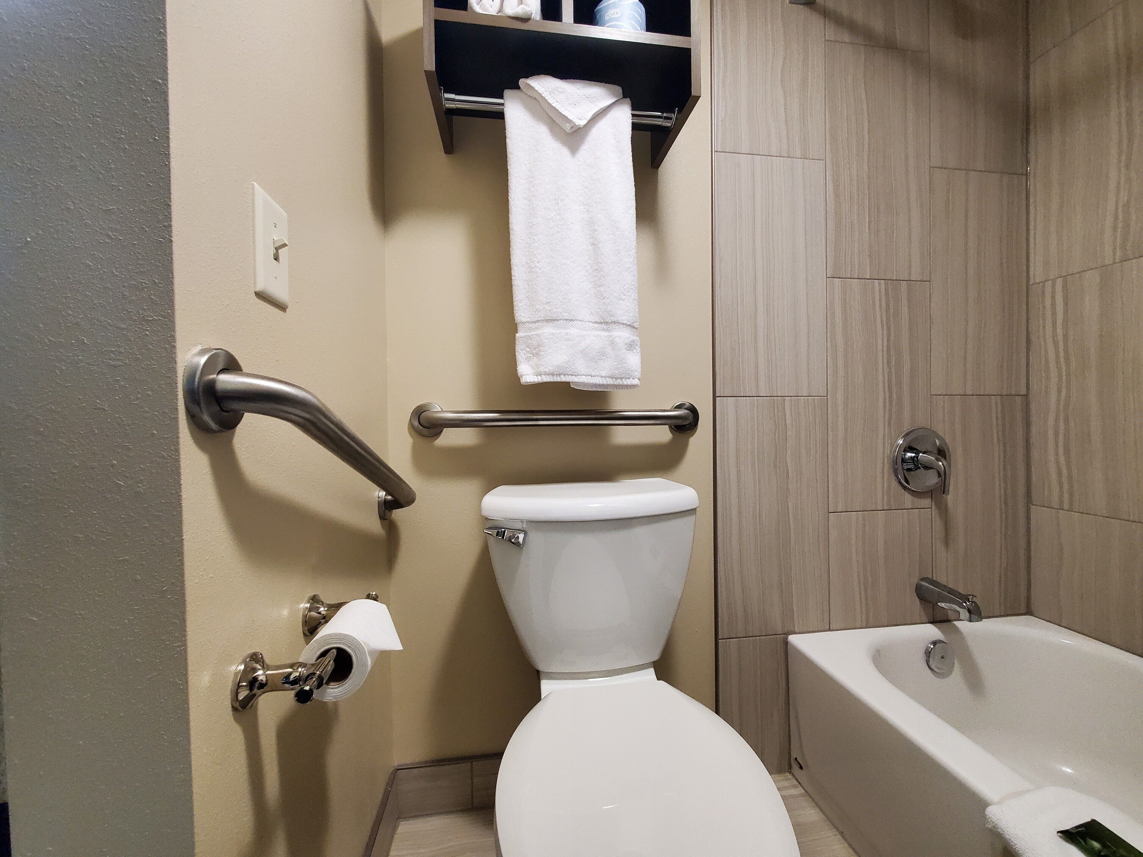 A bathroom with a toilet, a handrail, a towel rack, and a bathtub.