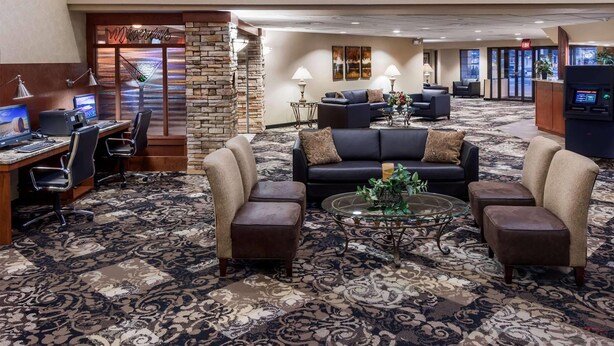 Un vestíbulo de hotel con una recepción, una zona de estar con sofás y sillones, una estación de computadoras y una pared decorativa con detalles de piedra.