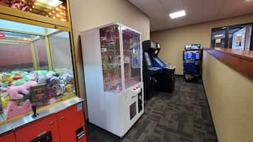 A hotel lobby with a claw machine filled with plush toys, a racing game machine, and a counter with a cash register.