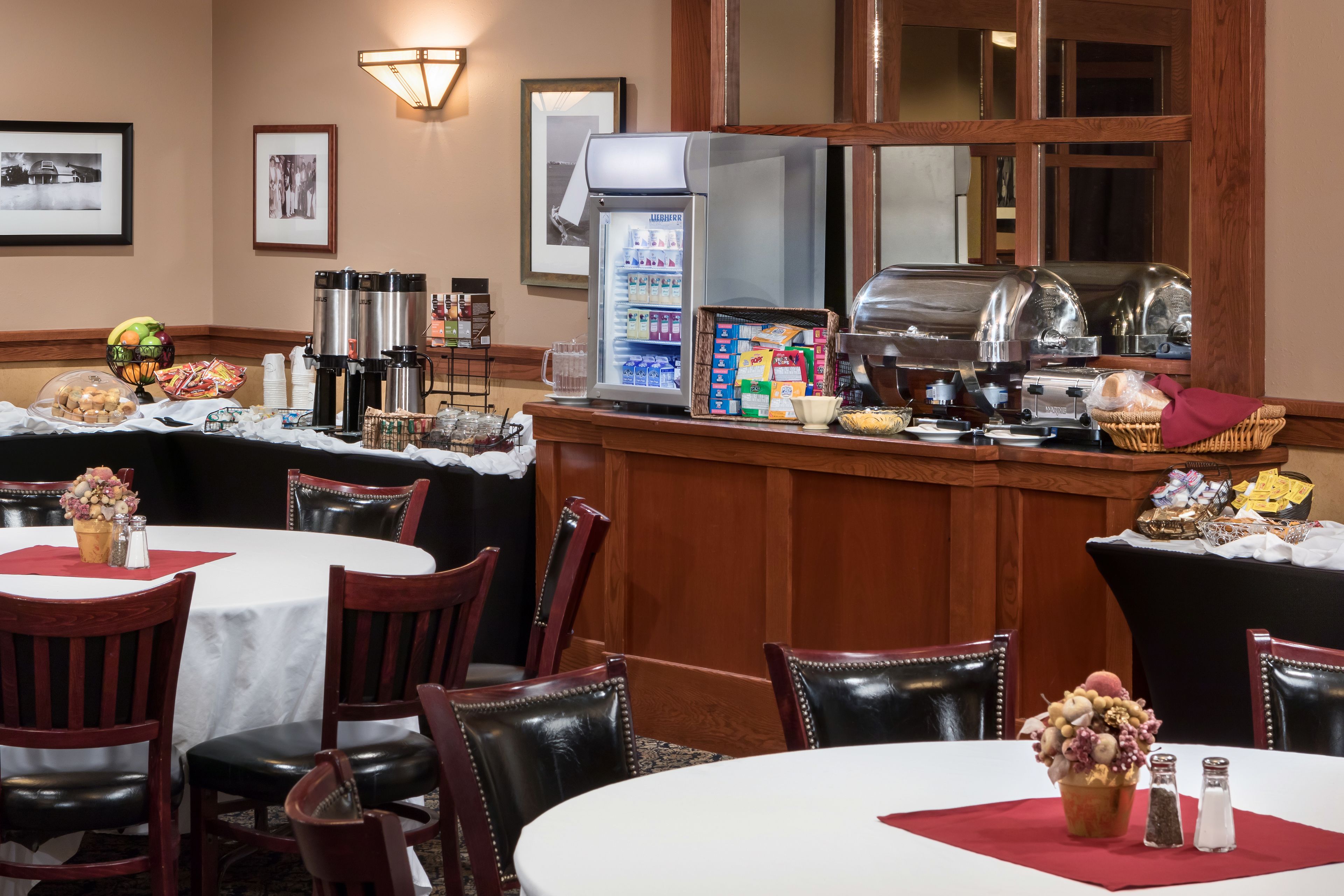 Un espace de restauration d’hôtel avec des tables rondes, des chaises, un buffet et un réfrigérateur rempli de boissons.