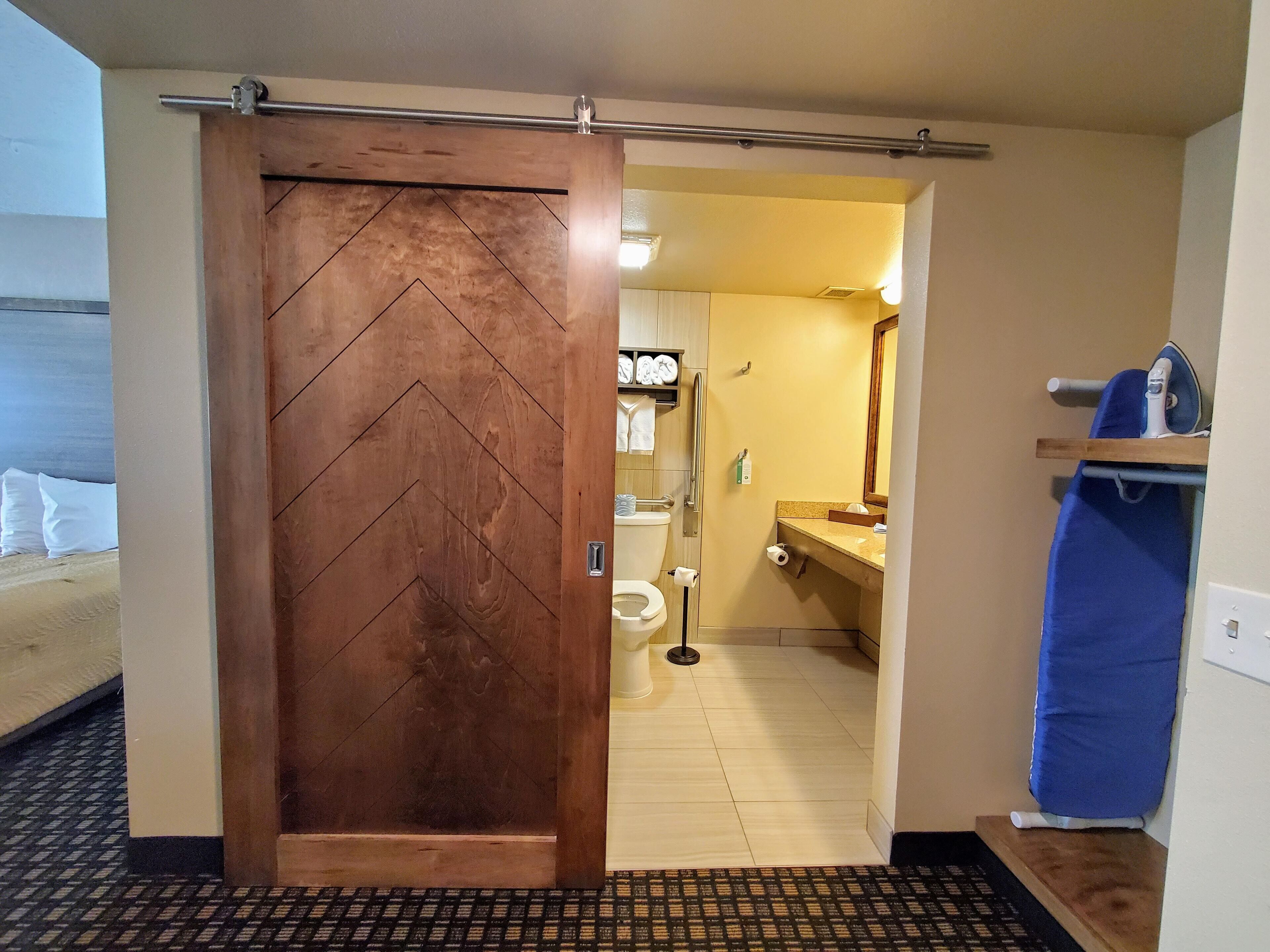 Ett hotellrum med en skjutdörr i trä, ett badrum med toalett, handfat och spegel.