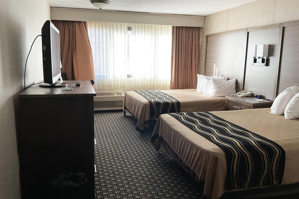 Une chambre d’hôtel avec deux lits, un bureau avec un ordinateur, un téléphone et une fenêtre avec des rideaux.