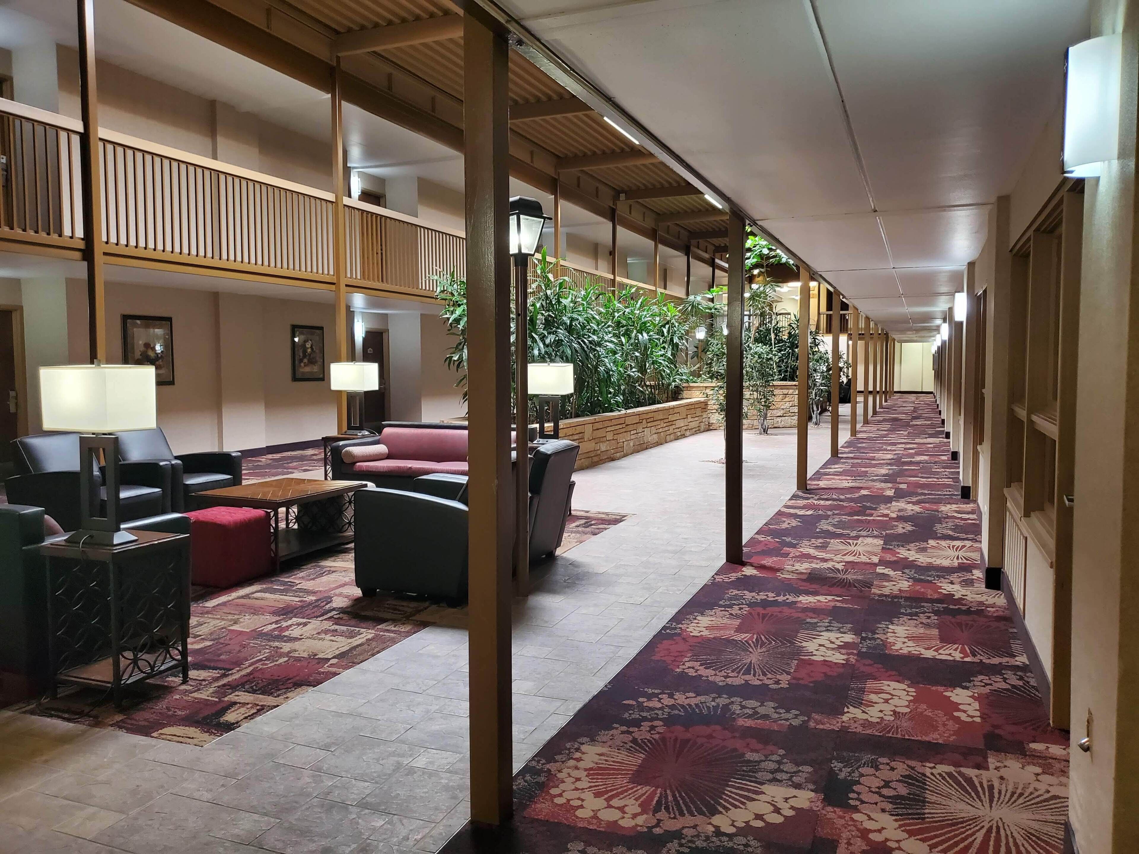 A hotel lobby with a long corridor, seating area with sofas and armchairs, and a patterned carpet.