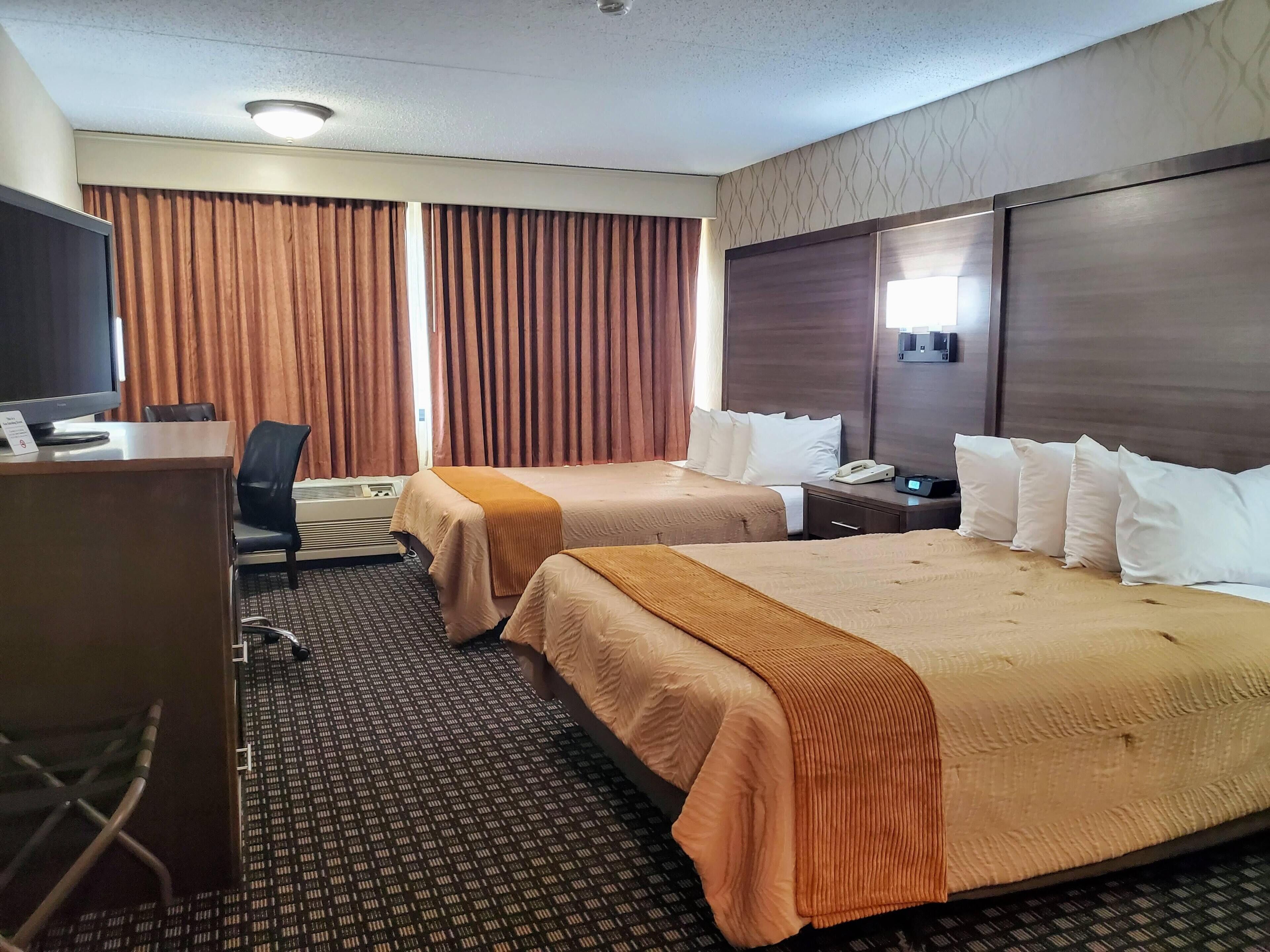 Une chambre d’hôtel avec deux lits, un bureau avec un ordinateur, une chaise et un téléviseur.