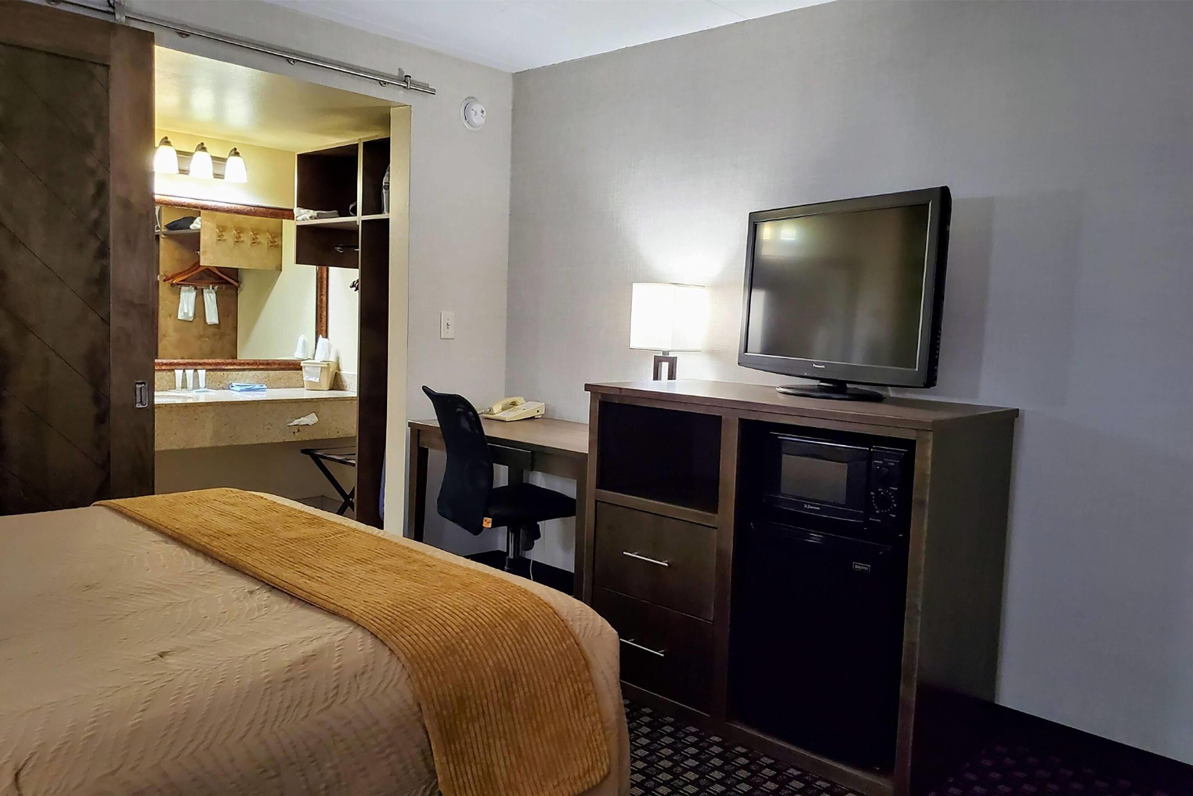 Een hotelkamer met een bed, een bureau met een computer, een televisie en een kledingkast.