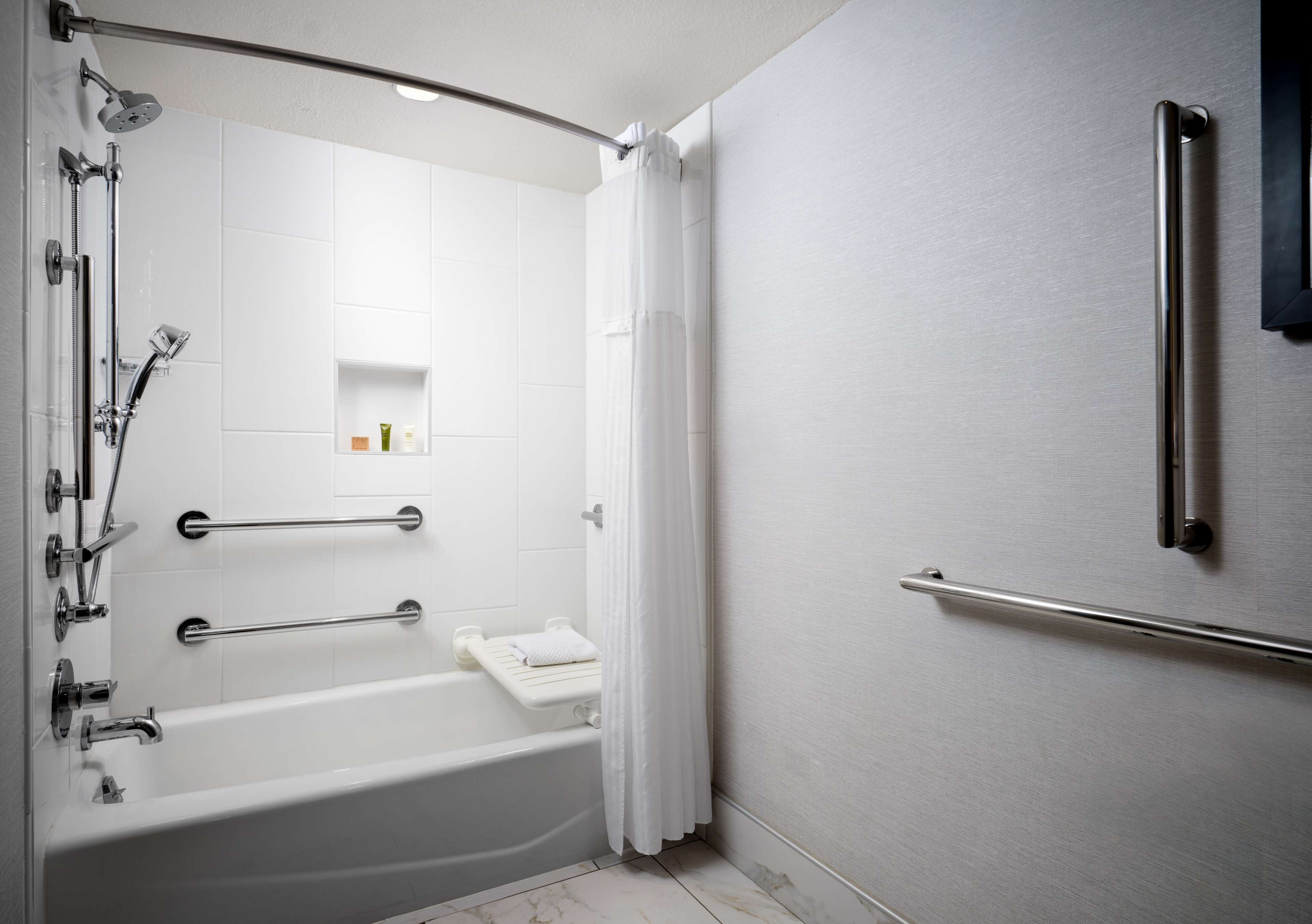 Un baño moderno con ducha a nivel, bañera con asiento integrado y barra de apoyo.