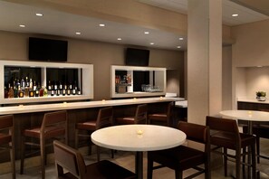 A bar area with multiple seating options, including round tables and bar stools, and a variety of bottles and glasses on shelves. - Hilton Fort Collins (Fort Collins)