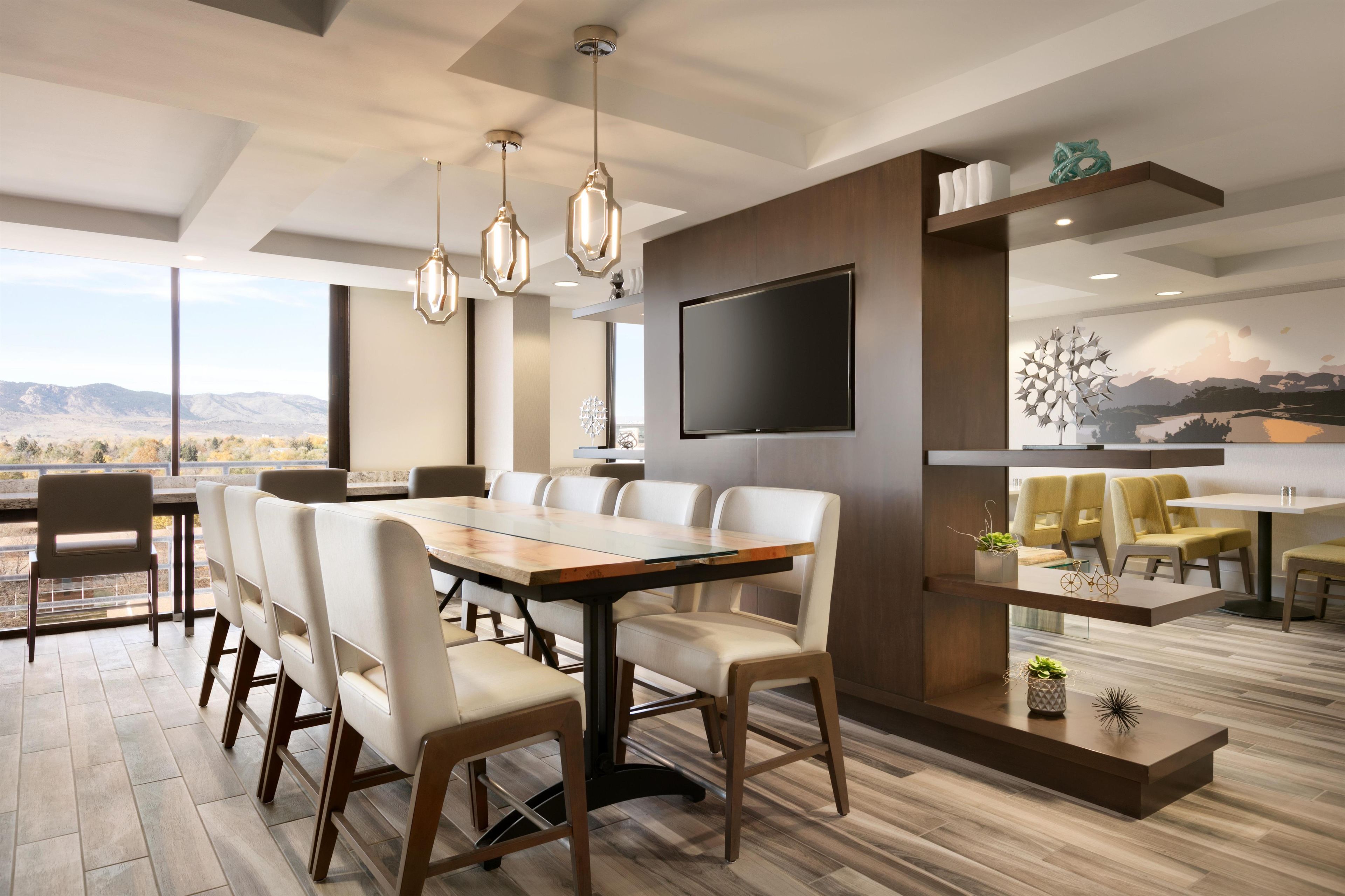 A modern dining area with a large table, chairs, and a flat-screen TV mounted on the wall.