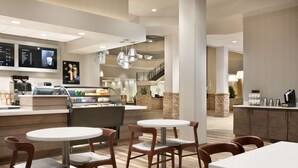 A modern hotel lobby with a coffee bar, seating area, and a staircase leading to an upper level. - Hilton Fort Collins (Fort Collins)