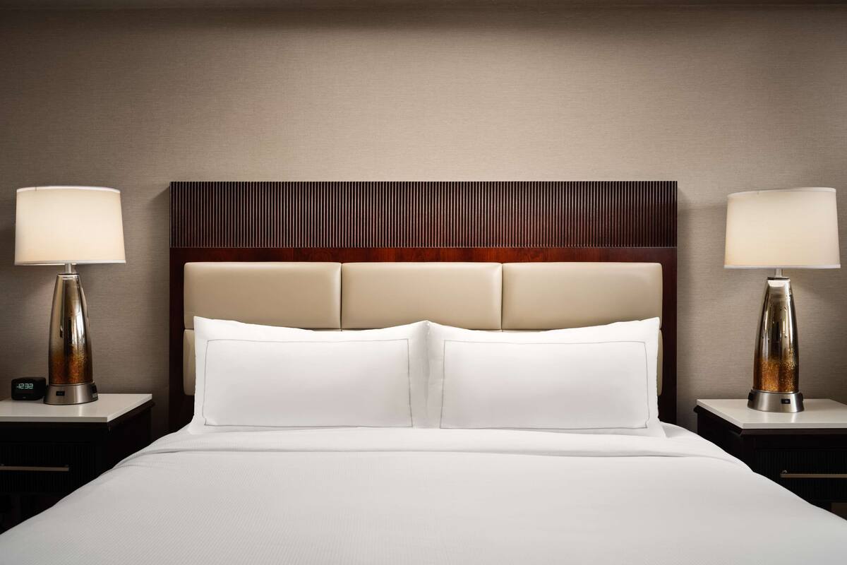 Quarto de hotel com uma cama grande, duas mesas de cabeceira e uma cabeceira com ripas verticais.