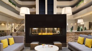 A spacious lobby with a central seating area, a stone accent wall, and a large window overlooking a fire feature. - Hilton Fort Collins (Fort Collins)