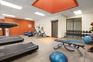 Un gimnasio con cintas de correr, elípticas, pesas libres y balones de ejercicios.